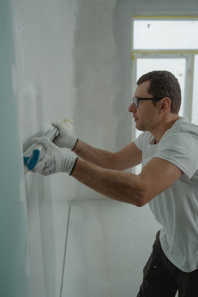Worker applying drywall compound during repairs after water damage in Plano, TX